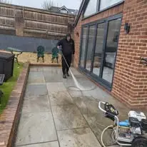 Man pressure washing a patio with bi-folds in background and pressure washer in foreground
